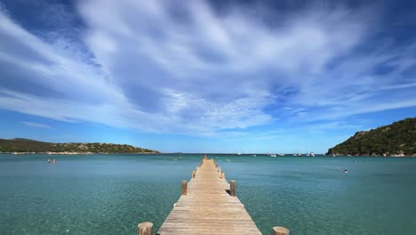 Moving-forward-over-long-wooden-pier-of-Santa-Giulia-famous-and-popular-beach-in-Corsica-with-pristine-azure-sea-water