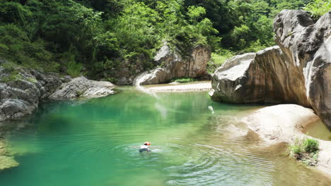 Aerial-shot-of-a-man-swimming-peacefully-in-a-calm,-magical-Nizao-river