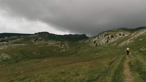 Pan-wide-angle-shot-revealing-a-hiker-crossing-a-mountain-alpine-valley-and-some-storm-clouds