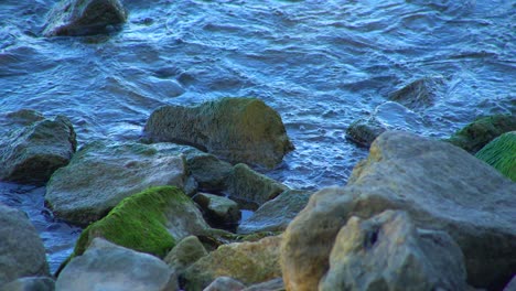 Waves-of-sea-crashing-into-mossy-stone,-close-up