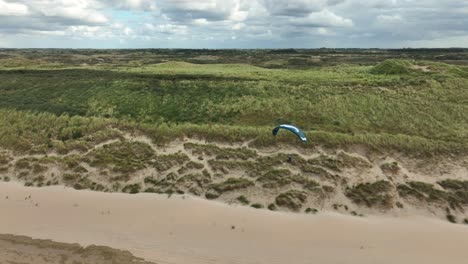 High-Speed-Aerial-Drone-Shot-Following-a-Person-Paragliding-Down-A-Beach-on-a-Sunny-day-in-Holland