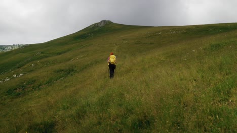Pan-wide-angle-shot-revealing-a-hiker-crossing-a-mountain-alpine-green-grass-meadow