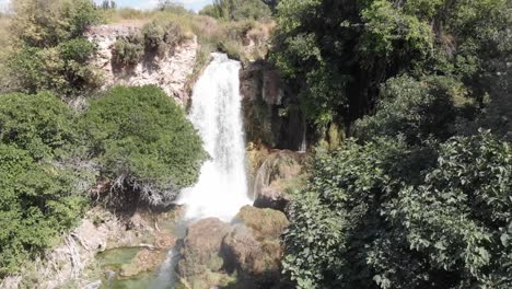 Wilder-Wasserfall,-Der-Von-Einem-Von-Bäumen-Umgebenen-Felsvorsprung-Fließt-Und-Einen-Regenbogen-Erzeugt