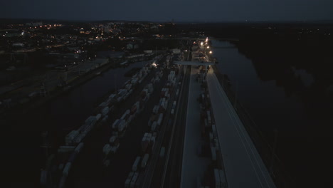 Luftaufnahme-Des-Schwach-Beleuchteten-Melnik-flusshafens-Mit-Containern-Und-Absetzern,-Die-In-Der-Nachtschicht-Arbeiten