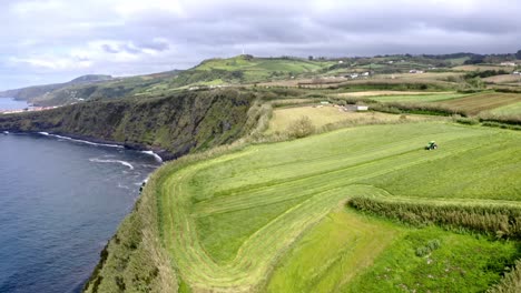 Tractor-working-in-farm-field-in-coastal-countryside,-Azores,-aerial