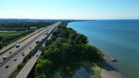 Aerial-parallel-to-busy-QEW-highway-over-Lake-Ontario-shore---Lincoln,-Ontario