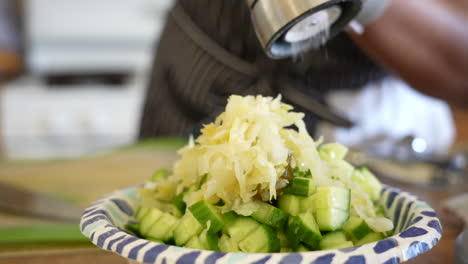 Grinding-salt-and-pepper-over-sauerkraut,-avocado,-and-cucumber-to-add-to-a-chopped-salad---ANTIPASTO-SALAD-SERIES