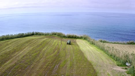 Tractor-cutting-grass-on-edge-of-sea-cliff,-Azores,-rotating-aerial
