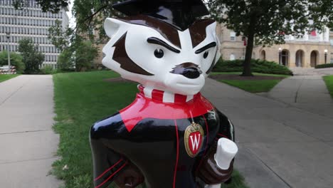 Bucky-Badger-mascot-statue-holding-diploma-on-the-campus-of-the-University-of-Wisconsin-in-Madison,-Wisconsin-with-gimbal-video-walking-forward