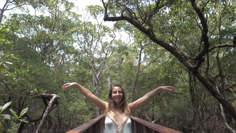 Sexy-Lady-Wearing-Dress,-Raises-Arms-While-Standing-On-Steel-Walkway-In-Daintree-Rainforest,-Queensland,-Australia