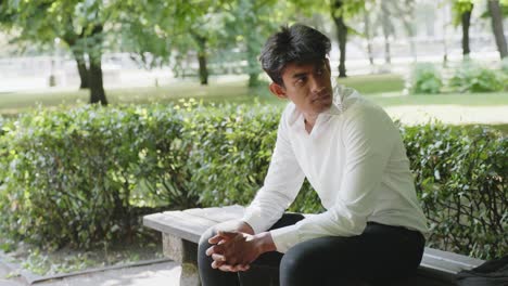 Handsome-Indian-entrepreneur-sitting-on-bench-in-park-on-warm-sunny-day