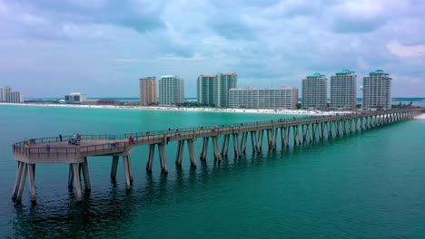 Drone-aerial-shot-for-the-end-of-the-Navarre-Beach-FL-pier-and-spinning-around-to-a-side-view-with-lots-of-hotels-on-the-white-sand-beach