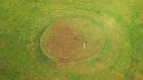 Cinematic-drone-shot-of-golf-course-green-with-flag-blowing-in-the-wind
