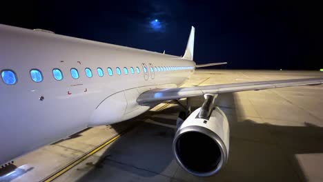 Unusual-night-wide-view-of-parked-airplane-in-airport-with-white-body-showing-fuselage-wing-engine-and-tail-with-moon-in-background