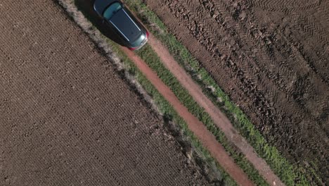 Aerial-top-down-view-of-an-SUV-driving-along-a-rural-dirt-road-between-fields