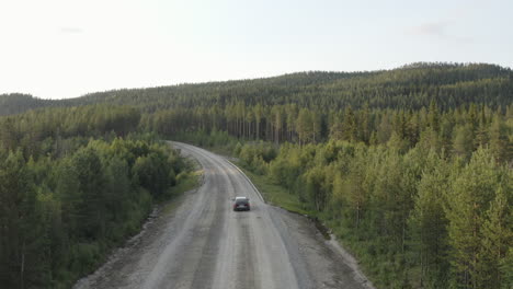 4k-Drone-shot-of-a-black-car-driving-alone-and-travel-on-empty-coutry-road-through-dense-forest