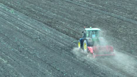 Drone-shot-of-tractor-plowing-agricultural-field-during-daytime---Dust-rising-up-to-sky