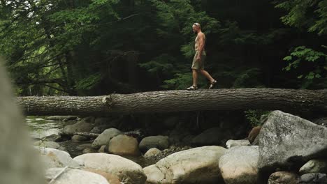 Guy-walking-shirtless-over-river-on-fallen-tree-bridge-super-slomo