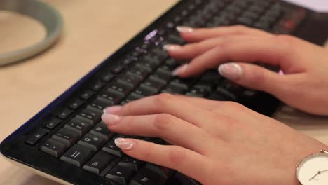 Young-girl-with-beautiful-fingernails-and-watch-typing-on-black-keyboard-on-computer-in-business