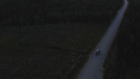 4k-Drone-shot-of-a-car-driving-on-a-country-road-at-dusk-through-forest-with-headlights