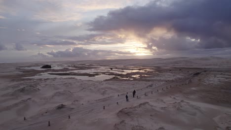 Cloudy-Sunset-Sky-Over-Wet-Sand-Dunes-Of-Stockton-Beach-In-New-South-Wales-With-Tourists-Revealed-In-Foreground