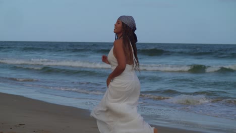 Young-girl-runs-on-the-beach-in-a-white-beach-dress-with-ocean-waves-crashing-at-her-feet-on-the-shoreline