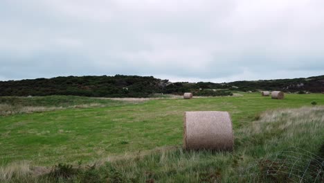 Countryside-meadow-with-rolled-straw-hay-bale-in-open-overcast-rural-British-farmland