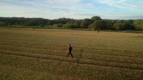 Man-traveling-alone-with-a-backpack-through-a-deserted-field-landscape-after-harvest