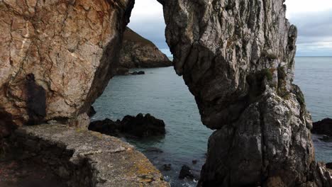 Looking-through-rock-arch-formation-out-to-Irish-sea-on-Traeth,-Porth-Wen-Beach