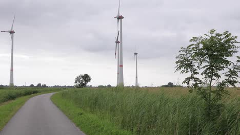 Kleine-Straße-Mit-Gras-Und-Windmühlen-Im-Hintergrund-An-Einem-Dunklen-Bewölkten-Tag