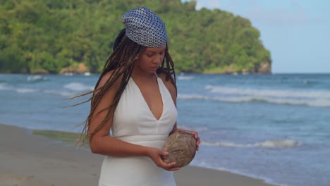 Young-woman-in-a-beach-dress-holds-a-dry-coconut-on-the-beach-on-a-tropical-Caribbean-island