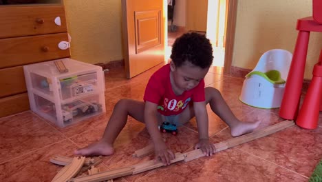 Schönes-Zweijähriges-Schwarzes-Kind,-Das-Sich-An-Eisenbahnschienen-Anschließt,-Um-Zu-Hause-Mit-Seiner-Spielzeugeisenbahn-Zu-Spielen