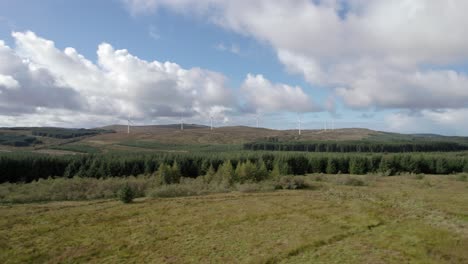 Aerial-drone-footage-slowly-rising-to-reveal-multiple-turning-wind-turbines-in-a-Scottish-windfarm-surrounded-by-forestry-plantations-of-commercial-conifers-on-the-Kintyre-Peninsula,-Argyll,-Scotland