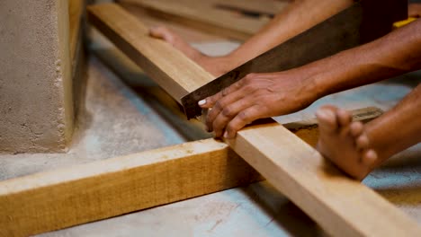Male-carpenter-cutting-wood-plank-with-hand-saw