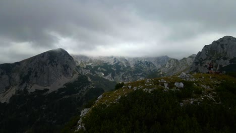 Drohnenaufnahmen,-Die-Bei-Schlechtem-Wetter-Rückwärts-über-Einen-Kleinen-Berg-Mit-Blick-Auf-Größere-Berge-Gehen,-Mit-Wolken,-Die-In-Slowenischen-Bergen-In-Den-Alpen-Gefilmt-Wurden