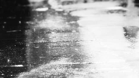 Light-rain-water-droplets-falling-onto-asphalt-road-reflecting-bright-light-on-dark-gloomy-day