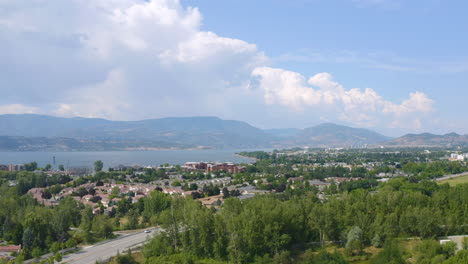 Aerial-view-of-Kelowna-homes-in-the-suburbs-on-a-sunny-day,-backing-up-to-reveal-fields-and-parks