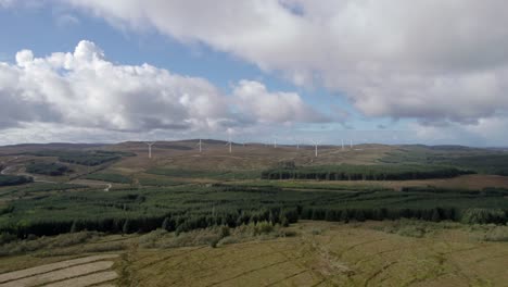 Aerial-drone-footage-rising-up-to-reveal-multiple-turning-wind-turbines-in-a-Scottish-windfarm-surrounded-by-forestry-plantations-of-commercial-conifers-on-the-Kintyre-Peninsula,-Argyll,-Scotland