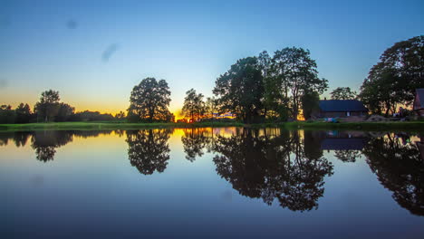 Zeitrafferaufnahme-Des-Wunderschönen-Sonnenuntergangs-Im-Hintergrund-über-Holzhütten-Neben-Einem-See-Während-Der-Abendzeit