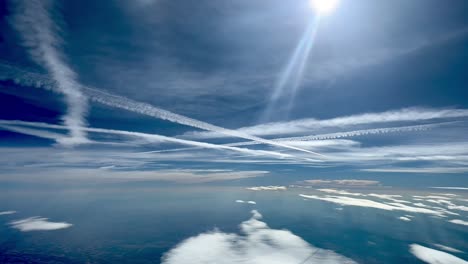 Busy-sky-with-the-wakes-of-crossing-jets-flying-at-high-levels,-with-a-deep-blue-sky-and-sun-flares-and-sunbeams