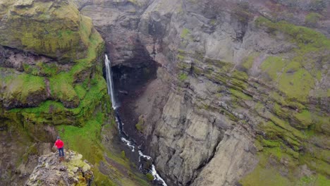 Canyon-waterfall-stationary-shot-of-red-jacket-hiker-admiring-view-of-green-canyon