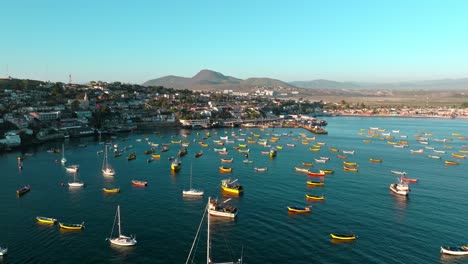 Dolly-in-aerial-view-of-several-yellow-fishing-boats-anchored-on-the-shore-of-the-Tongoy-peninsula,-Chile