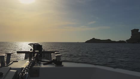 Perspektive-Vom-Segelbootbug-Mit-Strahlender-Sonne-Vor-Und-Felsen-Der-Insel-Korsika-Und-Leuchtturm-Capo-Pertusato-Im-Hintergrund,-Frankreich