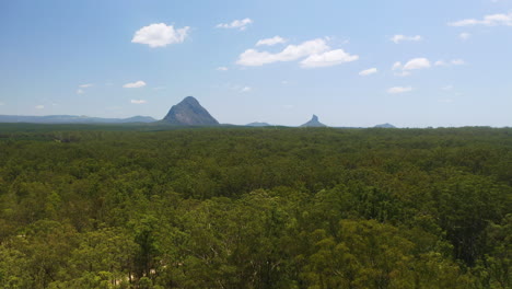Aerial-Drone-Over-Green-Australian-Trees-To-Reveal-Glasshouse-Mountain-Range-In-Distance,-4K
