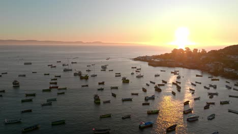 Zoom-in-aerial-view-of-fishing-boats-stopped-with-the-sunset-and-the-sun-in-the-background,-Tongoy,-Chile