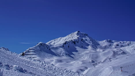 Zeitraffer-Schieberegleraufnahme-Eines-Schneebedeckten-Berges-Im-Skigebiet-Mit-Sessellift---Skifahrer,-Die-Bei-Perfekten-Bedingungen-Mit-Blauem-Himmel-Auf-Die-Abfahrt-Fahren