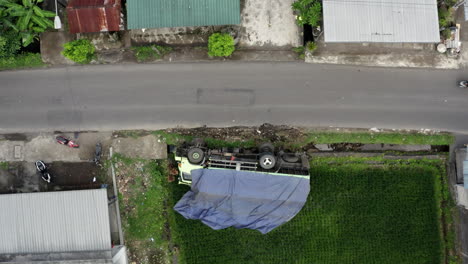 Overturned-truck-lying-on-side-next-to-narrow-road---Aerial-top-down-from-drone