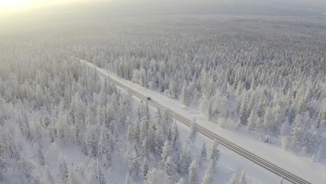 High-up-aerial-view-of-cars-driving-on-winter-road-surrounded-by-white-snowy-forest