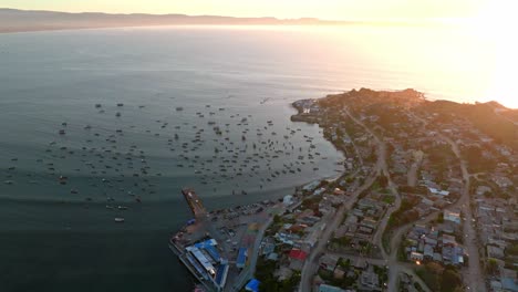Aerial-orbit-of-the-Tongoy-peninsula-with-several-fishing-boats-on-its-shore-with-the-sunset-and-the-sea-in-the-background,-Chile