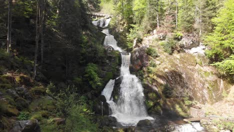 Hoher-Wasserfall,-Der-Auf-Felsen-Untergeht,-Und-Eine-Holzbrücke-Auf-Der-Spitze-Der-Kaskade